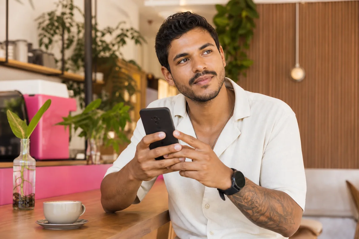 Homem brasileiro adulto pensando antes de responder uma conversa no celular.